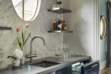 Example of a mid-sized transitional single-wall medium tone wood floor and brown floor wet bar design in Atlanta with an undermount sink, recessed-panel cabinets, blue cabinets, quartz countertops, multicolored backsplash, marble backsplash and gray countertops