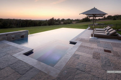 This is an example of a mid-sized transitional backyard rectangular infinity pool in Toronto with with a pool and natural stone pavers.