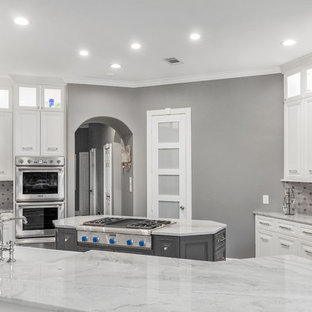 This is an example of a large transitional u-shaped kitchen pantry in Houston with a farmhouse sink, raised-panel cabinets, grey cabinets, quartzite benchtops, grey splashback, limestone splashback, stainless steel appliances, dark hardwood floors, a peninsula, brown floor and grey benchtop.
