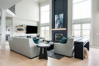 Ejemplo de sala de estar tipo loft minimalista grande con paredes grises, suelo de madera clara, todas las chimeneas y marco de chimenea de ladrillo