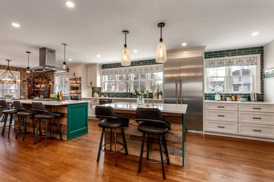 Photo of a large classic galley kitchen/diner in Columbus with a submerged sink, recessed-panel cabinets, engineered stone countertops, green splashback, ceramic splashback, stainless steel appliances, medium hardwood flooring, multiple islands, brown floors and white worktops.