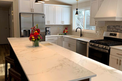 Inspiration for a large transitional l-shaped vinyl floor, brown floor and vaulted ceiling eat-in kitchen remodel in Milwaukee with an undermount sink, shaker cabinets, white cabinets, white backsplash, porcelain backsplash, an island and white countertops