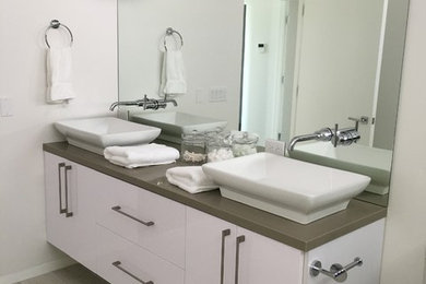 Mid-sized trendy 3/4 porcelain tile and beige floor bathroom photo in Los Angeles with flat-panel cabinets, white cabinets, a one-piece toilet, white walls, a vessel sink and solid surface countertops