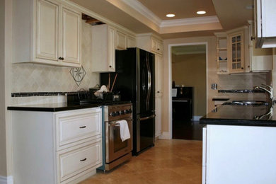 Example of a classic galley kitchen design in Orange County with raised-panel cabinets, white cabinets, granite countertops, beige backsplash, ceramic backsplash and black countertops