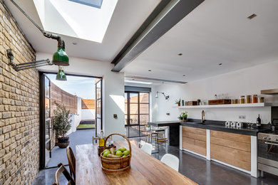 Mid-sized contemporary l-shaped eat-in kitchen in London with an integrated sink, flat-panel cabinets, medium wood cabinets, concrete benchtops, black splashback, cement tile splashback, panelled appliances, concrete floors and a peninsula.