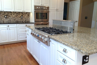 Mid-sized minimalist l-shaped medium tone wood floor eat-in kitchen photo in DC Metro with a double-bowl sink, raised-panel cabinets, white cabinets, granite countertops, multicolored backsplash, glass tile backsplash, stainless steel appliances and an island