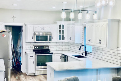 Kitchen - huge cottage laminate floor and brown floor kitchen idea in Omaha with a farmhouse sink, white cabinets, granite countertops, white backsplash, subway tile backsplash, stainless steel appliances, no island and white countertops
