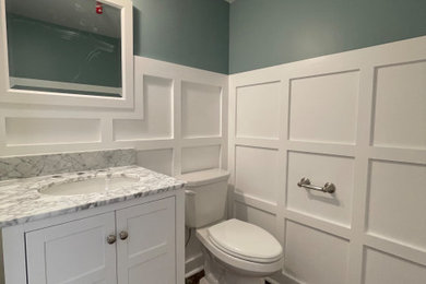 Example of a small arts and crafts dark wood floor and wall paneling powder room design in Philadelphia with flat-panel cabinets, white cabinets, a two-piece toilet, green walls, an integrated sink, quartz countertops, multicolored countertops and a freestanding vanity