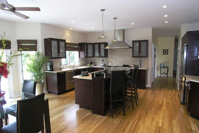 Eat-in kitchen - large transitional u-shaped light wood floor eat-in kitchen idea in New York with an undermount sink, shaker cabinets, dark wood cabinets, solid surface countertops, white backsplash, ceramic backsplash, stainless steel appliances and an island