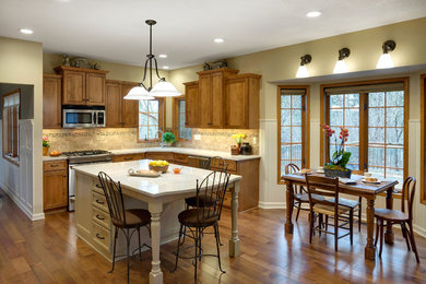 Mid-sized traditional u-shaped eat-in kitchen in Minneapolis with an undermount sink, recessed-panel cabinets, medium wood cabinets, quartzite benchtops, beige splashback, stone tile splashback, stainless steel appliances, light hardwood floors, with island and brown floor.