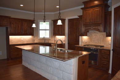 Kitchen - large transitional u-shaped dark wood floor and brown floor kitchen idea in Austin with an undermount sink, raised-panel cabinets, dark wood cabinets, granite countertops, beige backsplash, stone tile backsplash, stainless steel appliances and an island
