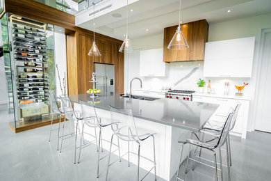 Large minimalist galley concrete floor kitchen photo in Calgary with flat-panel cabinets, white cabinets, white backsplash, stainless steel appliances, an island and stone slab backsplash
