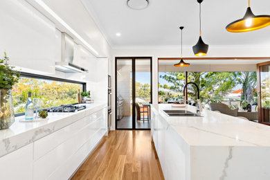 This is an example of a contemporary eat-in kitchen in Brisbane with a double-bowl sink, flat-panel cabinets, white cabinets, marble benchtops, window splashback, with island and white benchtop.