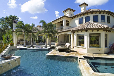 Large backyard custom-shaped lap pool in Tampa with a water feature and natural stone pavers.