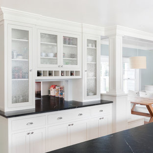 This is an example of a large contemporary kitchen pantry in Boston with a farmhouse sink, recessed-panel cabinets, white cabinets, soapstone benchtops, black splashback, stone slab splashback, stainless steel appliances, medium hardwood floors and with island.