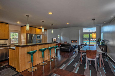 Large modern l-shaped open plan kitchen in Santa Barbara with dark hardwood floors, an undermount sink, stainless steel appliances, shaker cabinets, light wood cabinets, concrete benchtops, with island and brown floor.