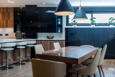 Modelo de cocina moderna abierta con fregadero integrado, puertas de armario negras, encimera de cuarzo compacto, salpicadero blanco, electrodomésticos de acero inoxidable, suelo laminado, península, suelo marrón y encimeras blancas