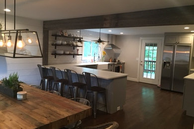Inspiration for a mid-sized cottage l-shaped medium tone wood floor eat-in kitchen remodel in New York with a farmhouse sink, shaker cabinets, gray cabinets, quartz countertops, white backsplash, porcelain backsplash, stainless steel appliances and a peninsula