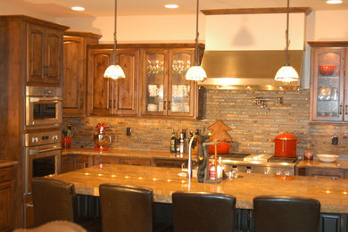 Inspiration for a large rustic l-shaped eat-in kitchen remodel in Denver with raised-panel cabinets, dark wood cabinets, granite countertops, multicolored backsplash, stone tile backsplash, stainless steel appliances, an island and brown countertops