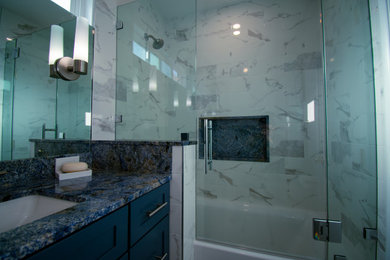 サンフランシスコにある高級な小さなトランジショナルスタイルのおしゃれな浴室 (シェーカースタイル扉のキャビネット、青いキャビネット、ドロップイン型浴槽、シャワー付き浴槽	、一体型トイレ	、白いタイル、磁器タイル、白い壁、磁器タイルの床、アンダーカウンター洗面器、御影石の洗面台、白い床、開き戸のシャワー、青い洗面カウンター、ニッチ、洗面台1つ、造り付け洗面台) の写真