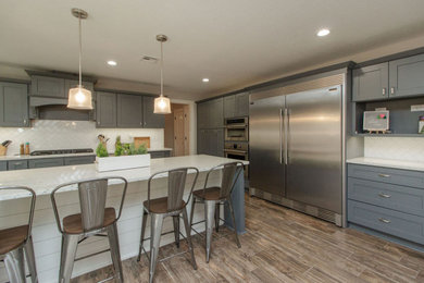 Example of a huge farmhouse l-shaped brown floor open concept kitchen design in Other with recessed-panel cabinets, blue cabinets, granite countertops, white backsplash, stainless steel appliances, an island and white countertops