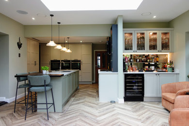 Design ideas for a large traditional open plan kitchen in West Midlands with a double-bowl sink, shaker cabinets, distressed cabinets, quartz worktops, white splashback, engineered quartz splashback, black appliances, vinyl flooring, an island, brown floors, white worktops and feature lighting.