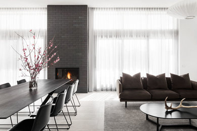 This is an example of a contemporary dining room in Melbourne with white walls, ceramic floors, a standard fireplace, a brick fireplace surround and grey floor.