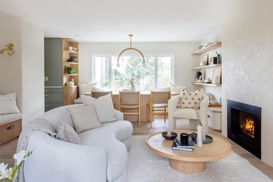 Example of a mid-sized trendy open concept medium tone wood floor and brown floor living room design in Vancouver with white walls, a standard fireplace, a plaster fireplace and a wall-mounted tv