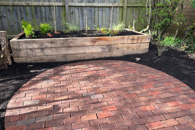 This is an example of a medium sized classic back partial sun garden for spring in Other with a raised bed, brick paving and a wood fence.