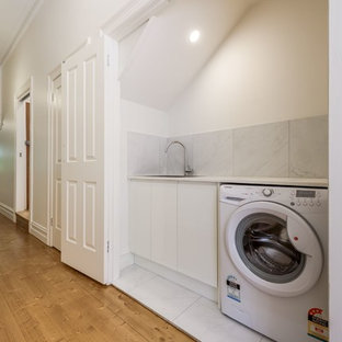 メルボルンの小さいモダンスタイルのおしゃれな家事室 (ドロップインシンク、ルーバー扉のキャビネット、白いキャビネット、御影石カウンター、白い壁、セラミックタイルの床、白い床、白いキッチンカウンター) の写真