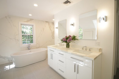 Photo of a mid-sized transitional bathroom in New York with flat-panel cabinets, white cabinets, a freestanding tub, a one-piece toilet, gray tile, porcelain tile, grey walls, porcelain floors, an undermount sink and engineered quartz benchtops.
