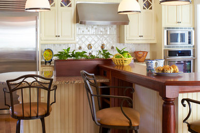 Eat-in kitchen - mid-sized craftsman l-shaped medium tone wood floor and brown floor eat-in kitchen idea in Boston with a double-bowl sink, raised-panel cabinets, yellow cabinets, granite countertops, white backsplash, ceramic backsplash, stainless steel appliances and an island