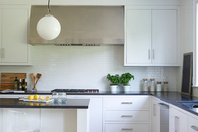 Example of a trendy l-shaped medium tone wood floor kitchen design in New York with an undermount sink, flat-panel cabinets, white cabinets, white backsplash, stainless steel appliances and an island
