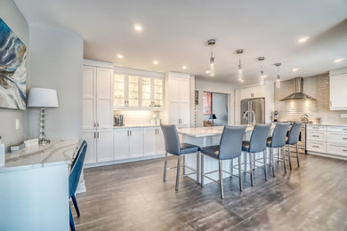 Example of a large trendy l-shaped porcelain tile and gray floor eat-in kitchen design in Ottawa with a double-bowl sink, recessed-panel cabinets, white cabinets, quartz countertops, beige backsplash, glass tile backsplash, stainless steel appliances, an island and multicolored countertops