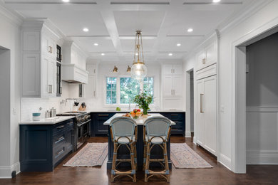 Elegant u-shaped dark wood floor and brown floor kitchen photo in Chicago with an undermount sink, recessed-panel cabinets, white cabinets, white backsplash, paneled appliances, an island and white countertops