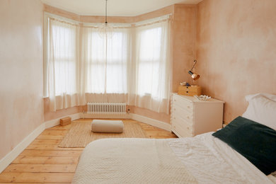 Photo of a scandi master bedroom in London with pink walls, medium hardwood flooring and brown floors.