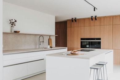 This is an example of a large contemporary eat-in kitchen in Munich with an undermount sink, flat-panel cabinets, light wood cabinets, limestone benchtops, beige splashback, limestone splashback, black appliances, with island, beige floor and beige benchtop.