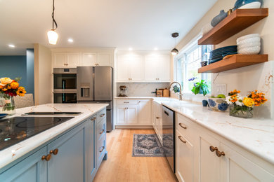 Example of a mid-sized transitional l-shaped light wood floor eat-in kitchen design in Bridgeport with a farmhouse sink, shaker cabinets, white cabinets, quartz countertops, white backsplash, quartz backsplash, stainless steel appliances, an island and white countertops
