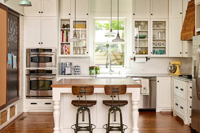 Inspiration for a large country u-shaped eat-in kitchen in Charlotte with a farmhouse sink, raised-panel cabinets, white cabinets, stainless steel benchtops, white splashback, subway tile splashback, stainless steel appliances, medium hardwood floors and with island.