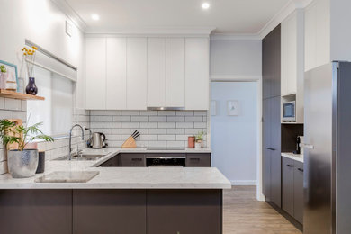 Photo of a mid-sized modern u-shaped eat-in kitchen in Adelaide with a drop-in sink, grey cabinets, laminate benchtops, white splashback, subway tile splashback, stainless steel appliances, bamboo floors, brown floor and white benchtop.