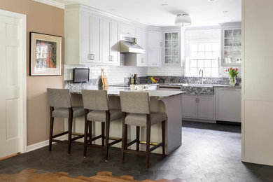 Inspiration for a mid-sized transitional u-shaped slate floor and black floor open concept kitchen remodel in New York with a farmhouse sink, recessed-panel cabinets, gray cabinets, quartzite countertops, white backsplash, ceramic backsplash, stainless steel appliances and an island
