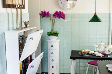 This is an example of a mid-sized eclectic galley separate kitchen in Berlin with a drop-in sink, white cabinets, wood benchtops, green splashback, glass tile splashback, stainless steel appliances, linoleum floors, black floor and black benchtop.
