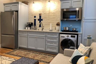This is an example of a small transitional single-wall open plan kitchen in Other with recessed-panel cabinets, grey cabinets, no island, an undermount sink, marble benchtops, white splashback, brick splashback, stainless steel appliances, light hardwood floors, brown floor and grey benchtop.