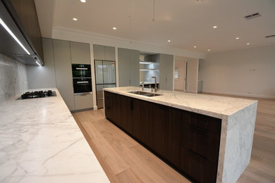 Large contemporary l-shaped kitchen pantry in Sydney with an undermount sink, flat-panel cabinets, grey cabinets, marble benchtops, white splashback, marble splashback, black appliances, with island and white benchtop.