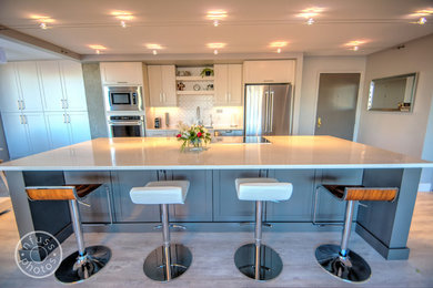 Mid-sized minimalist single-wall light wood floor eat-in kitchen photo with an undermount sink, beaded inset cabinets, white cabinets, stainless steel appliances, an island, quartzite countertops, white backsplash and mosaic tile backsplash