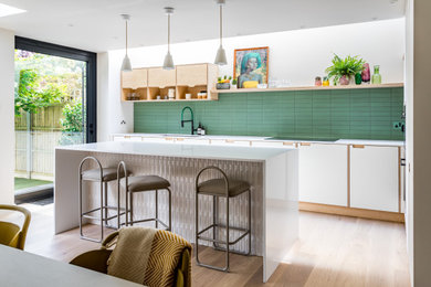 Design ideas for a contemporary galley kitchen in London with a submerged sink, flat-panel cabinets, white cabinets, green splashback, light hardwood flooring, an island, beige floors and white worktops.