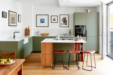 Moderne Küche in L-Form mit Landhausspüle, flächenbündigen Schrankfronten, grünen Schränken, schwarzen Elektrogeräten, braunem Holzboden, Kücheninsel, braunem Boden und weißer Arbeitsplatte in Berlin