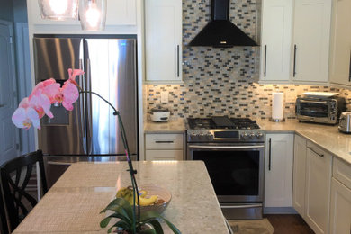 Mid-sized beach style u-shaped medium tone wood floor and brown floor open concept kitchen photo in Orlando with an undermount sink, white cabinets, quartzite countertops, multicolored backsplash, mosaic tile backsplash, stainless steel appliances, an island and beige countertops