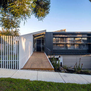 Photo of a large modern two-storey grey house exterior in Melbourne with metal siding, a flat roof and a metal roof.