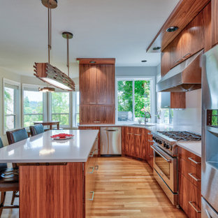 Exemple d'une grand cuisine ouverte tendance en L avec un évier encastré, un placard à porte plane, des portes de placard en bois sombre, un plan de travail en quartz modifié, une crédence blanche, une crédence en quartz modifié, un électroménager en acier inoxydable, un sol en bois clair, un îlot central, un sol marron et un plan de travail blanc.